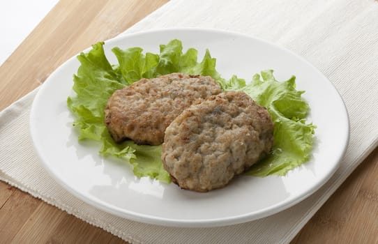 White plate with two rissoles and green lettuce on the napkin on the wooden board