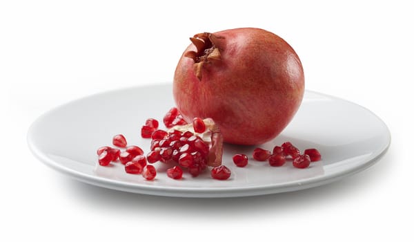 One whole red pomegranate with seeds on the white plate