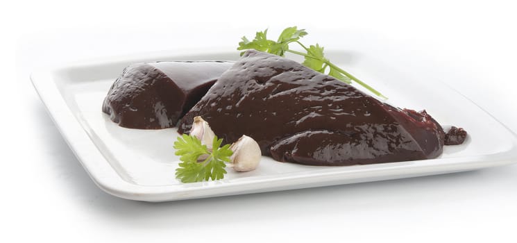 Two pieces of raw liver with garlic clove and parsley on the white plate