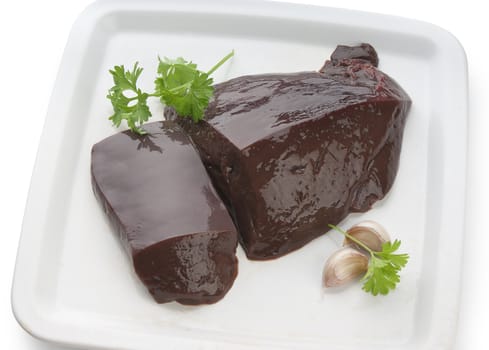 Two pieces of raw liver with parsley and garlic clove on the white plate