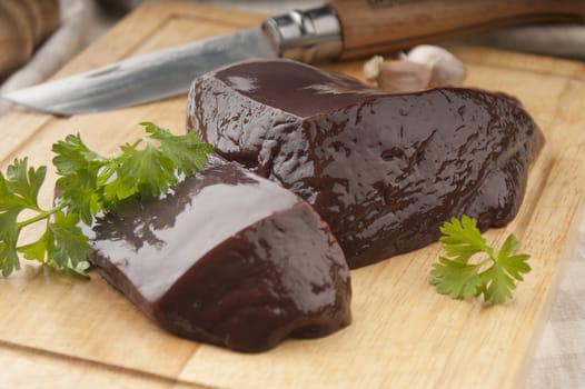 Two raw pieces of liver on the wooden board with parsley, garlic and knife