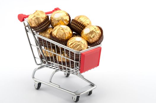 Shopping cart full of chocolates on white background