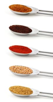 Spices measured in metal teaspoons, isolated on a white background: chinese five spice, ground cloves, smoked paprika, mustard seeds, ground cumin.