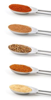 Spices measured in metal teaspoons, isolated on a white background: paprika, ground cinnamon, whole cumin seeds, ground mace and ground ginger.