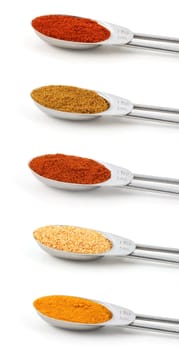 Spices measured in metal teaspoons, isolated on a white background: chilli powder, curry powder, cayenne, garlic granules and turmeric.