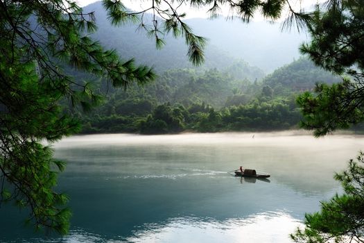 Fishing boat on the foggy river with tree branch as the foreground, in hunan province of China