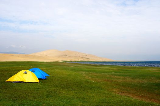 Tent on the lawn near the lake and sand dunes in qinghai province of China