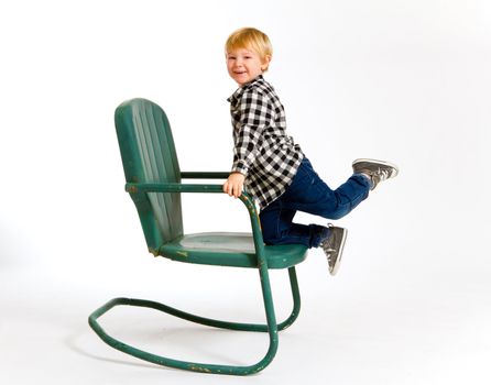 A boy in a plaid shirt has a fun time playing on this green rocking chair against an isolated white background in the studio.