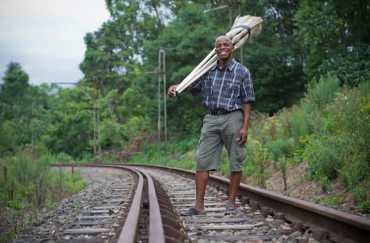 Stock photograph of a black South African entrepreneur small business broom salesman on railway line in Hilton, Pietermaritzburg, Kwazulu-Natal