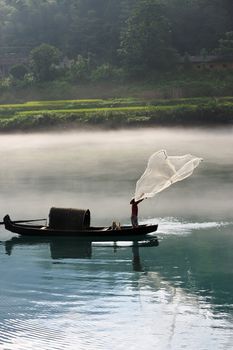 A fisherman casting his net from the boat on the river