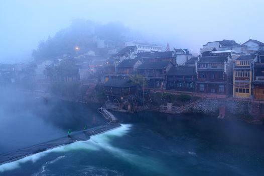 Foggy river landscape with Chinese traditional wooden buildings as background