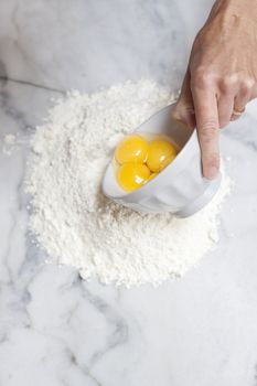 A hand holds a bowl with eggs being poured into flour