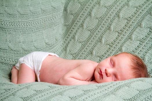 A young newborn baby boy rests wrapped up in a blanket and looking comfortable and cozy.