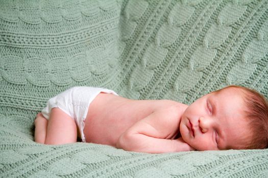 A young newborn baby boy rests wrapped up in a blanket and looking comfortable and cozy.