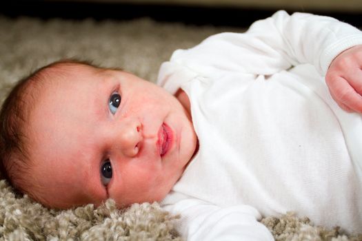 A baby newborn boy with his eyes open while resting on his side in a white outfit.