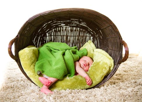 A baby boy sleeping on his side in a basket with a green blanket on a comfortable rug at his parents house.