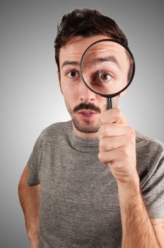 man looking through a magnifying lens on gray background