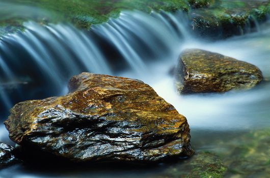 A paiur of river rocks with a small waterfall flowing behind them