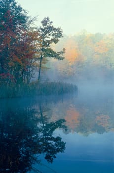 Smal pond with trees in fall color reflecting through the mist