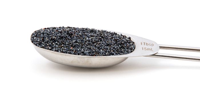 Poppy seeds measured in a metal tablespoon, isolated on a white background