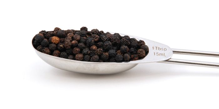 Black peppercorns measured in a metal tablespoon, isolated on a white background