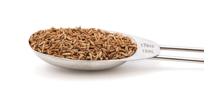 Cumin seeds measured in a metal tablespoon, isolated on a white background