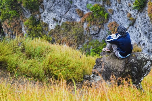 Young man sitting on mountain rock by the cliff