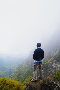 Young man in foggy mountain standing on a rock by the cliff