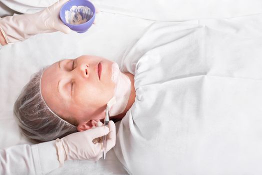Woman on the procedure in the beauty salon, applying a facial mask.