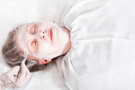 Woman on the procedure in the beauty salon, applying a facial mask.