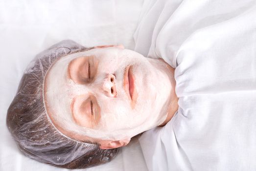 Attractive woman with facial mask lies in spa salon.