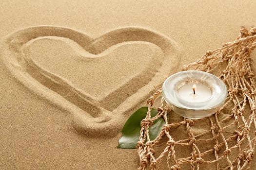handwritten heart on yellow soft sand with lighted candles
