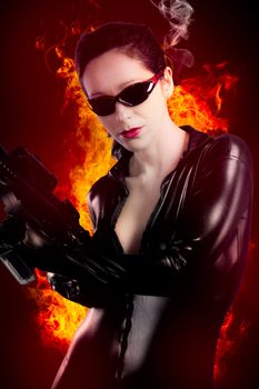 Sexy brunette woman in latex jumpsuit with heavy gun over fire background