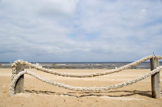 fence made of logs and thick rope on seaside beach sand and sea ocean in background.
