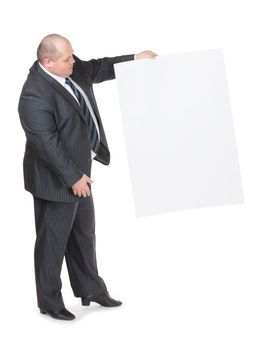 Cheerful overweight stylish business man in a suit holding up a blank white sign and pointing to it with his finger on a white studio background