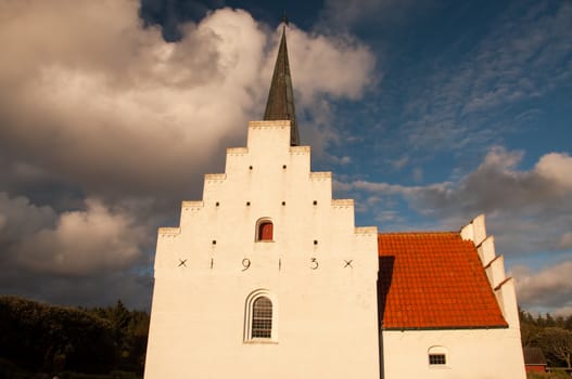 A white church in evening sun with dramatic clouds