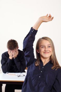 Photo of two students in class, one with a raised hand to answer a question and the other frustrated.
