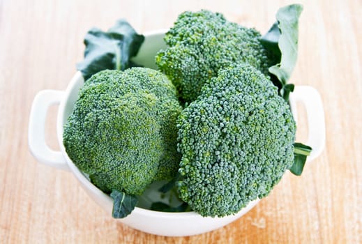 Fresh uncooked broccoli in colander and chopping board