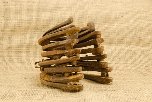heap of old retro rusty horseshoes on burlap material background.