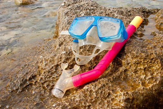 Blue snorkel goggle and tube on a rock near the sea