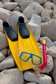 Yellow flippers with snorkel goggle and tube on a rock near the sea