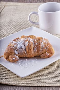 Full view of croissant with white cup on the back