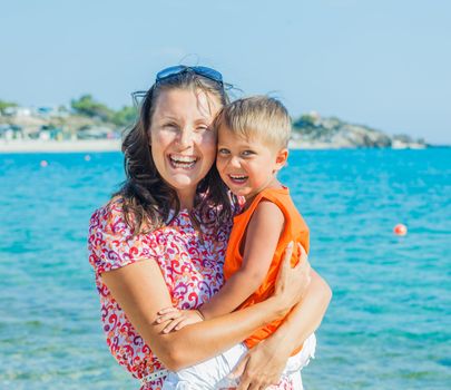 Clouseup portrait of happy mother with son laughing and looking at camera on the beach