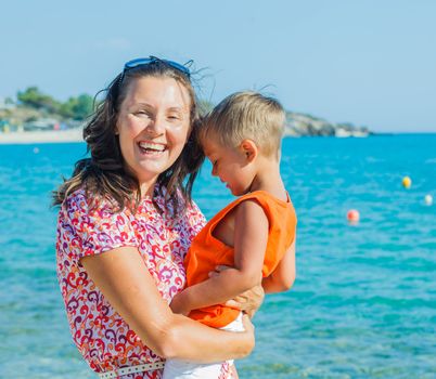 Clouseup portrait of happy mother with son laughing and looking at camera on the beach