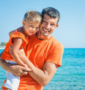 Clouseup portrait of happy father with son laughing and looking at camera on the beach