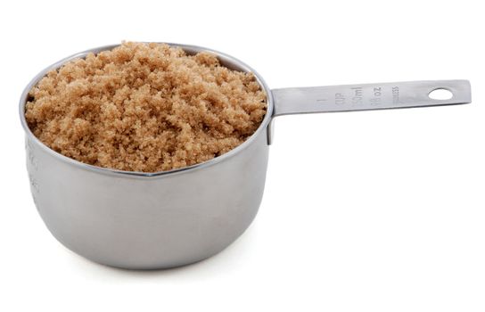 Light brown soft / muscovado sugar presented in an American metal cup measure, isolated on a white background