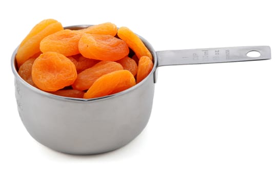 Whole dried apricots presented in an American metal cup measure, isolated on a white background