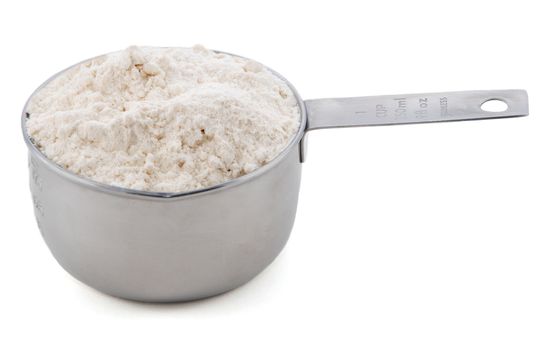 Plain / all purpose flour presented in an American metal cup measure, isolated on a white background