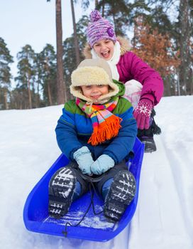 Cute sister and brother on sleds in snow forest. Focus on the boy