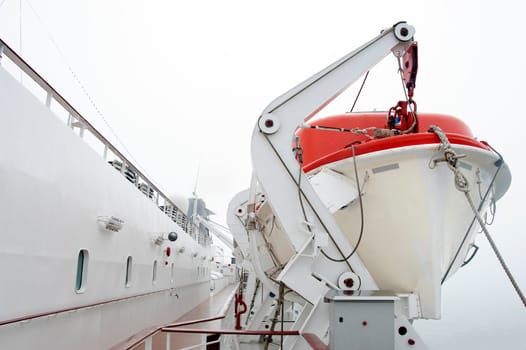 A Lifeboat on a passenger cruise ship hangs ready to launch in foggy weather.